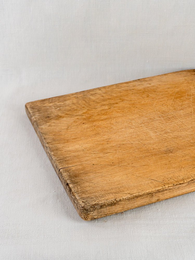 Large antique French hardwood chopping board with aged patina and wear, on a light fabric surface.