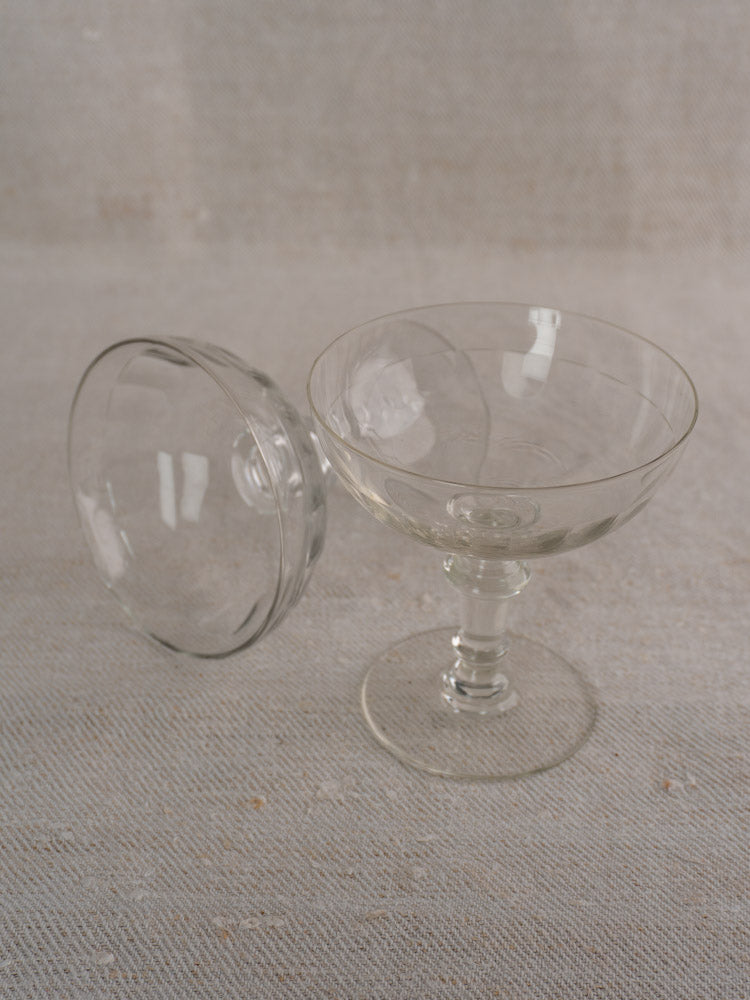 Pair of antique French hand-blown Champagne coupes, late 19th century, on a light textured surface.