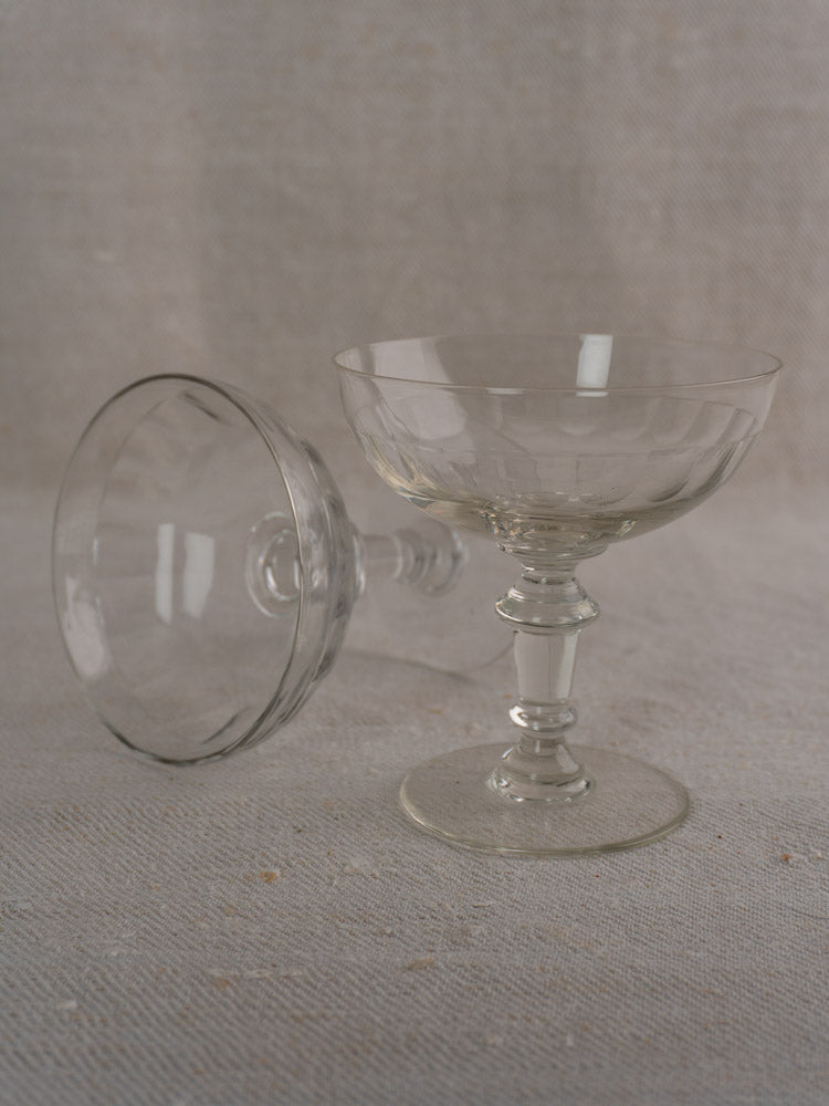 Pair of antique French champagne coupes, hand blown, one upright and one sideways on neutral textured fabric.