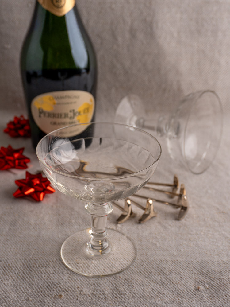 Pair of antique French hand-blown champagne coupes with bottle, red gift bows, and vintage keys on a textured surface.