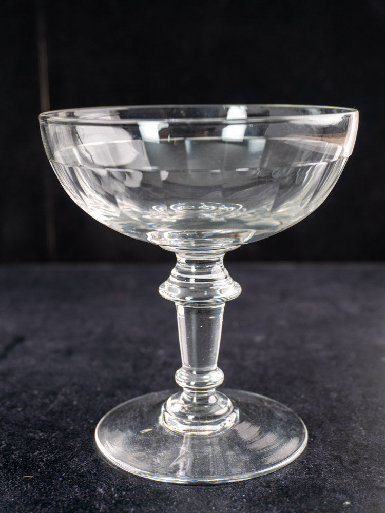 Pair of late 19th-century hand blown French Champagne coupes with short stems on a dark textured surface.