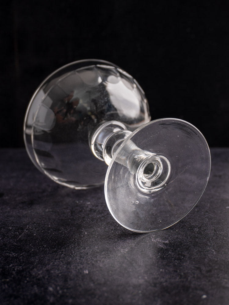 Pair of late 19th-century French antique glass champagne coupes resting on a dark textured surface with black background.
