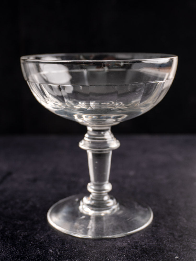 Pair of antique French hand-blown champagne coupes with wide bowls and short stems on a dark surface.