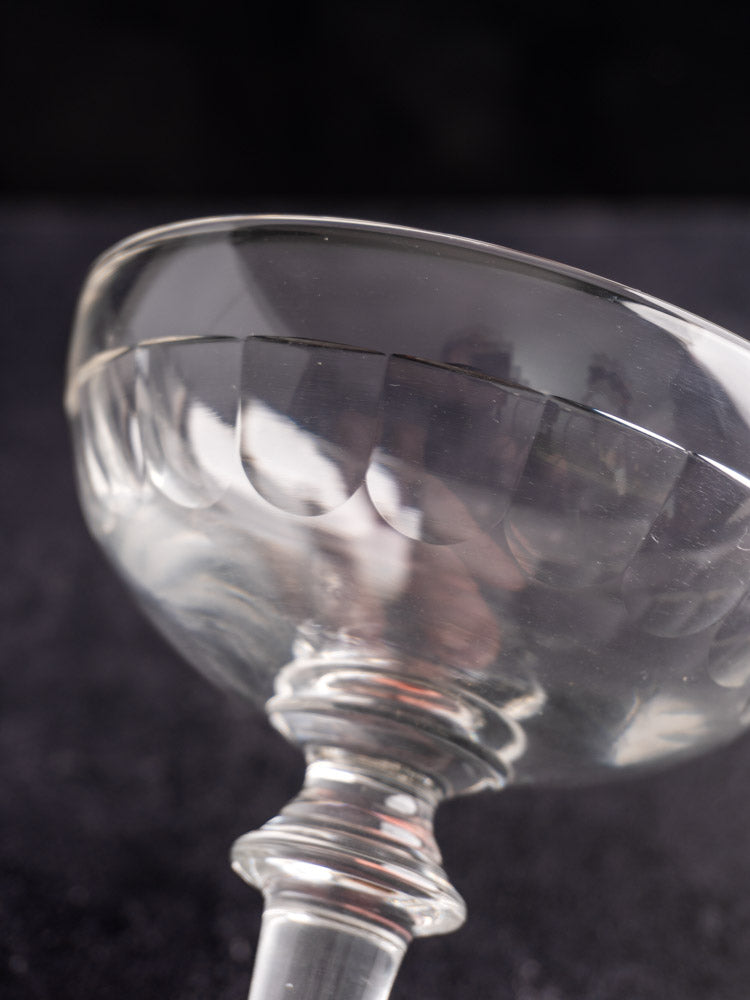 Antique French hand-blown champagne coupes with patterned rims, late 19th century, on a dark blurred background.