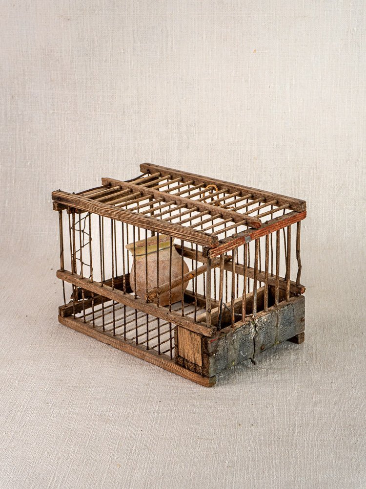 Antique French folk art bird cage, early 20th-century handcrafted wood and wire piece with rustic, weathered patina on neutral fabric.