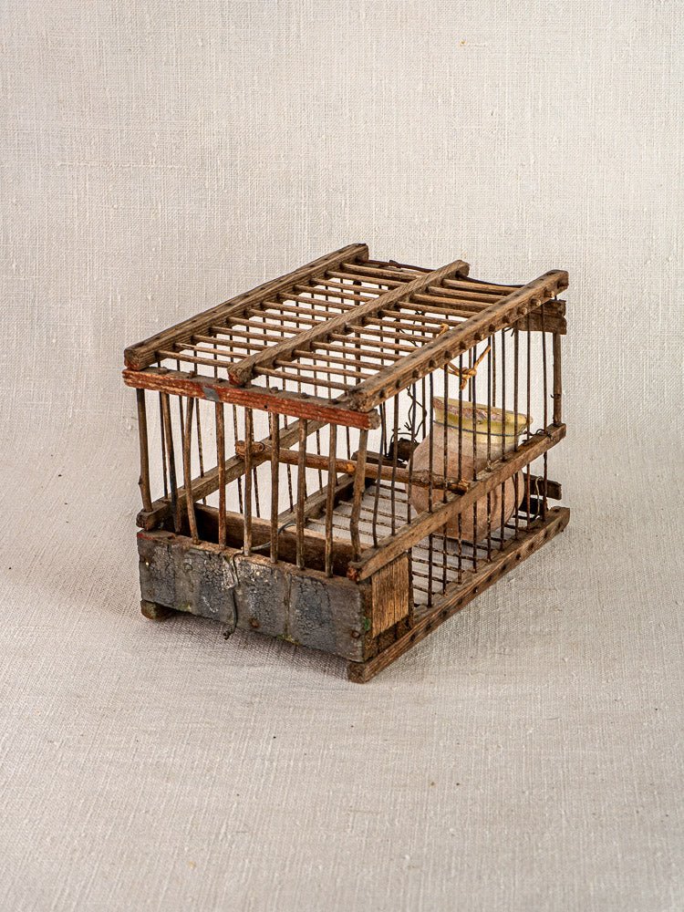 Antique French folk art bird cage, handmade from wood and wire, with perch and aged patina on textured fabric.
