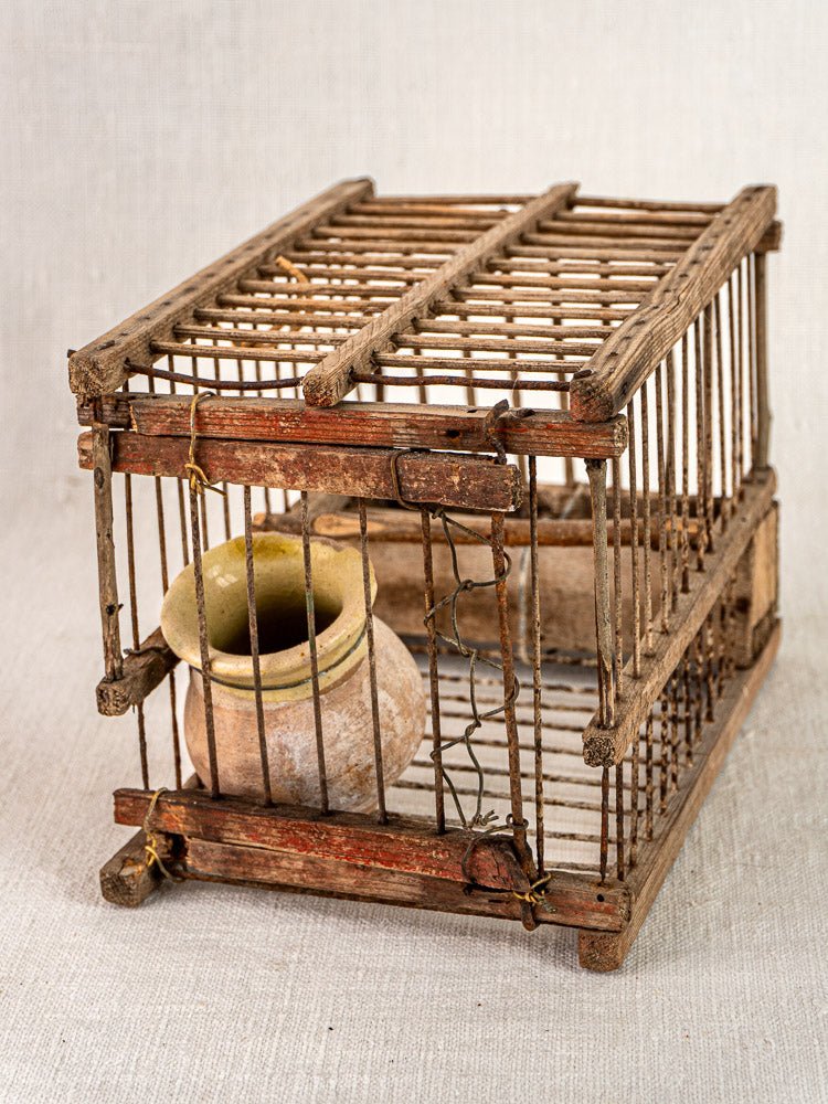 Antique French folk art bird cage, early 20th-century wood and wire with clay pot, on textured fabric.