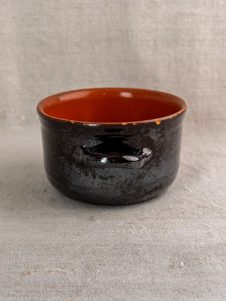 Albisola glazed earthenware Italian cooking pot with dark brown finish and single handle on textured fabric surface.