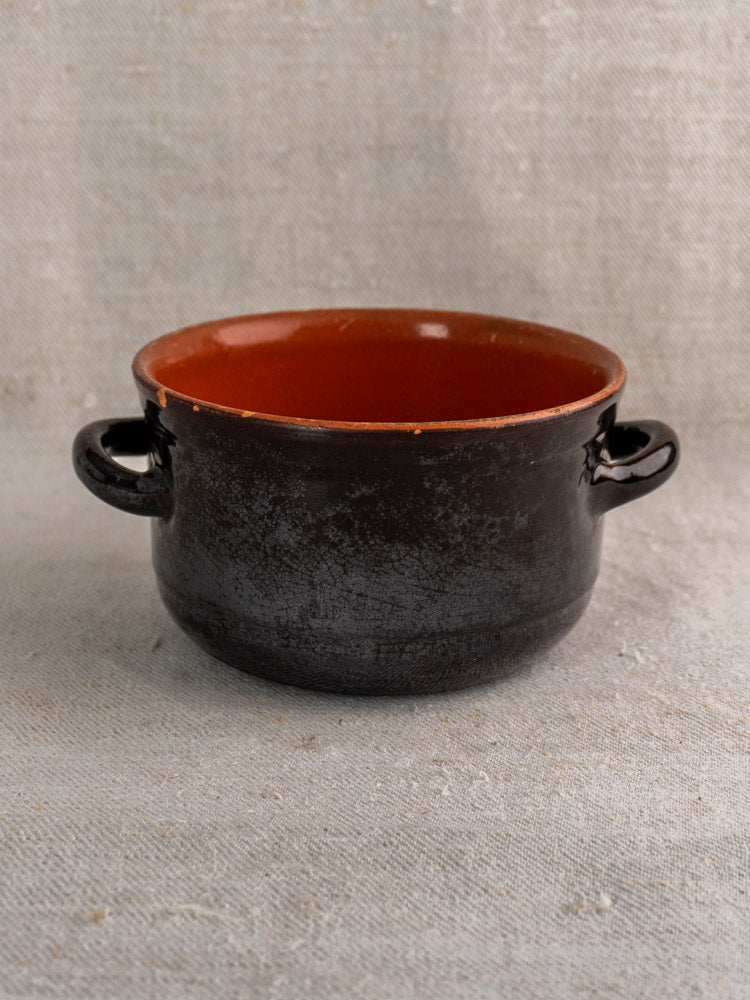 Albisola glazed Italian earthenware cooking pot, dark brown with reddish-brown interior, on textured beige fabric.