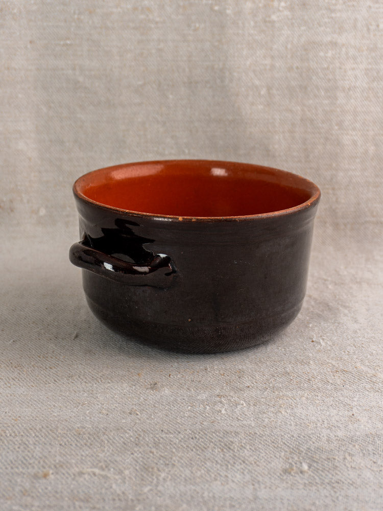 Vintage Italian glazed earthenware cooking pot by Coop. Stov., Albisola, dark brown with orange interior, on beige textured fabric.