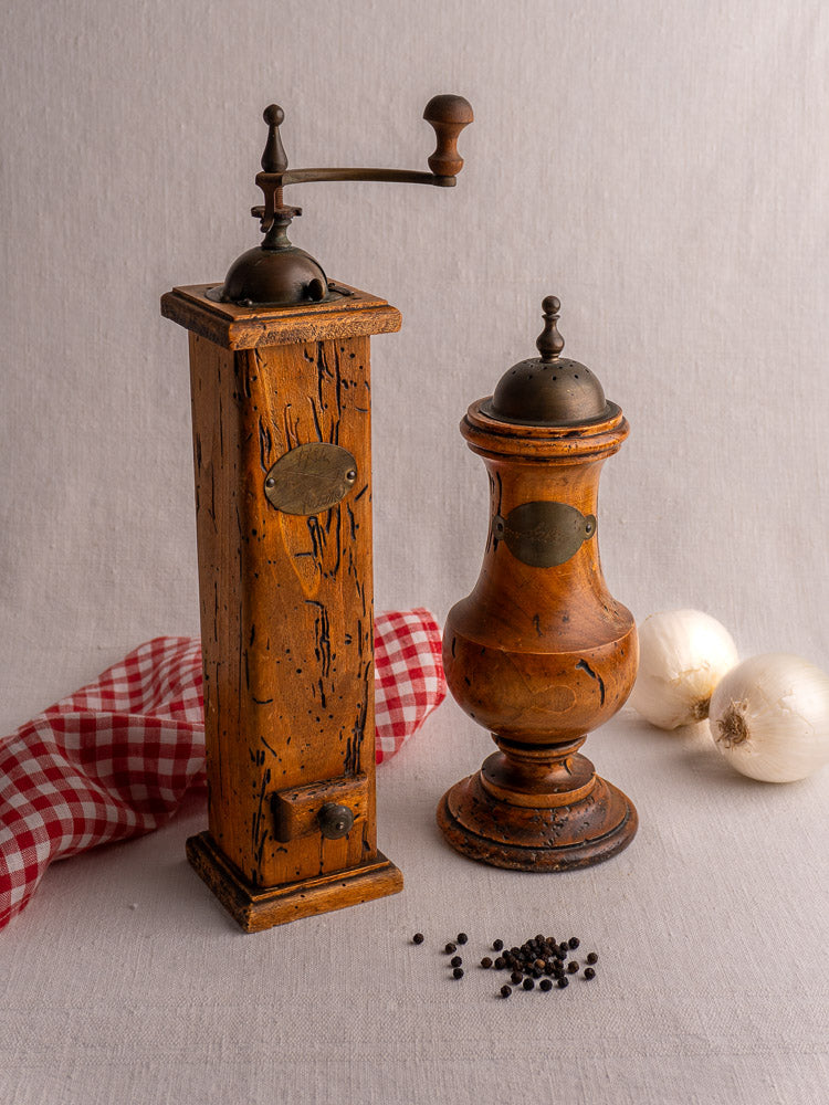 Antique Italian pepper mill and salt set by Stefano Ugolini Firenze on light cloth with peppercorns and white onions.