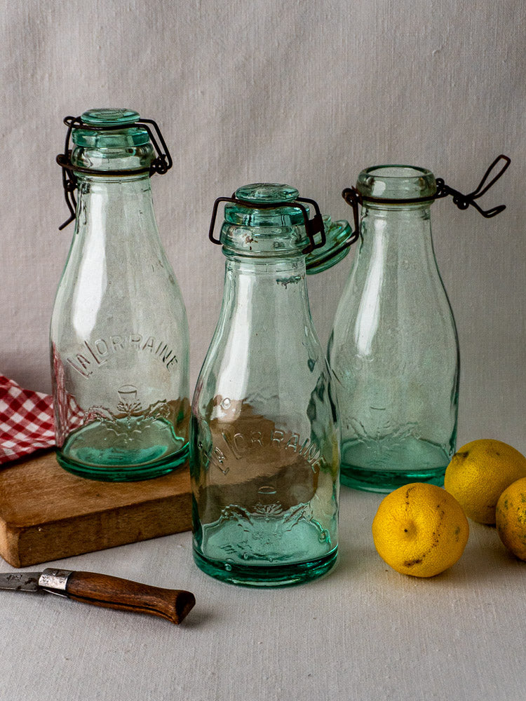 Set of three antique French La Lorraine aqua glass preserving bottles with lemons and kitchen accents.