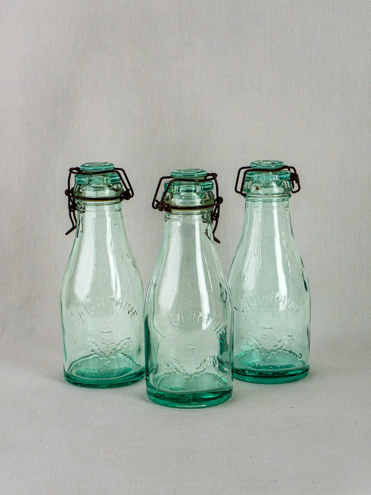 Set of three antique French La Lorraine aqua glass preserving bottles with embossed details and metal flip-top closures.