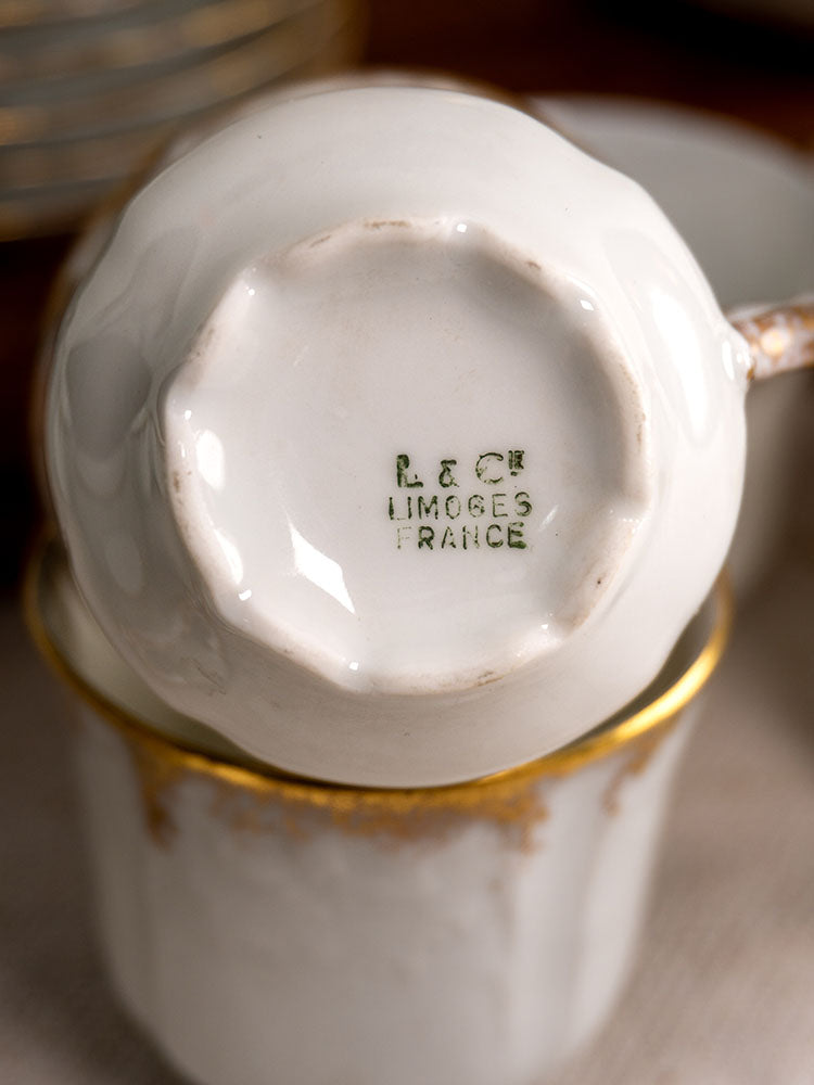 White porcelain cup bottom with green R&C Limoges France stamp, gold-trimmed demitasse cups arranged nearby.