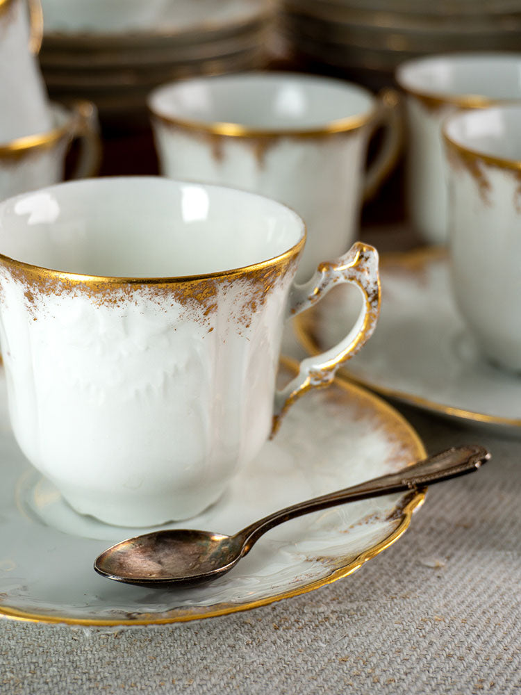 White French Limoges demitasse cup with gold trim on saucer, silver spoon, more cups behind.