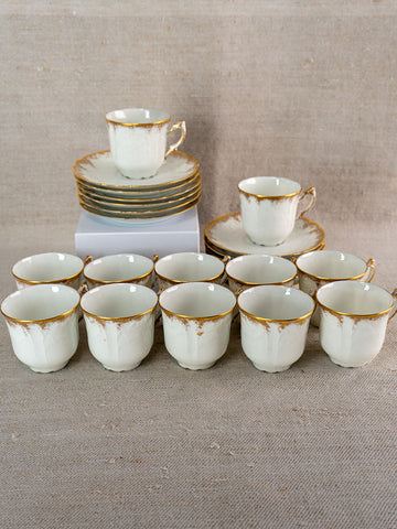 Antique French Limoges porcelain demitasse service with gold-trimmed cups, saucers on beige fabric.