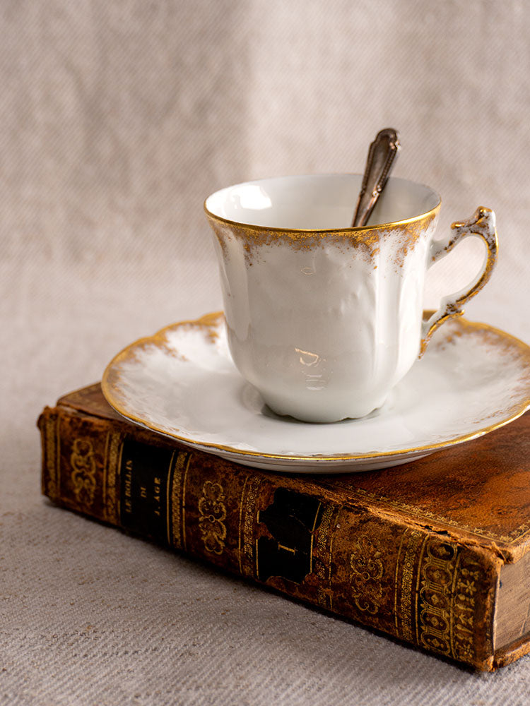 Antique French Limoges porcelain demitasse cup and saucer with gold rim on ornate leather book.
