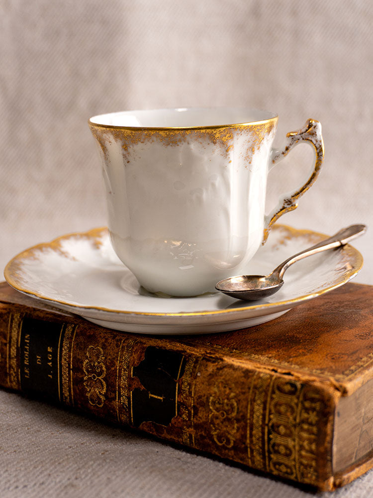 Antique French Limoges demitasse cup and saucer with gold trim, silver spoon, on vintage book.