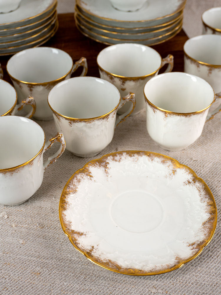 Antique French Limoges Lafarge & Cie demitasse service of 12, white with gold trim, on beige tablecloth.