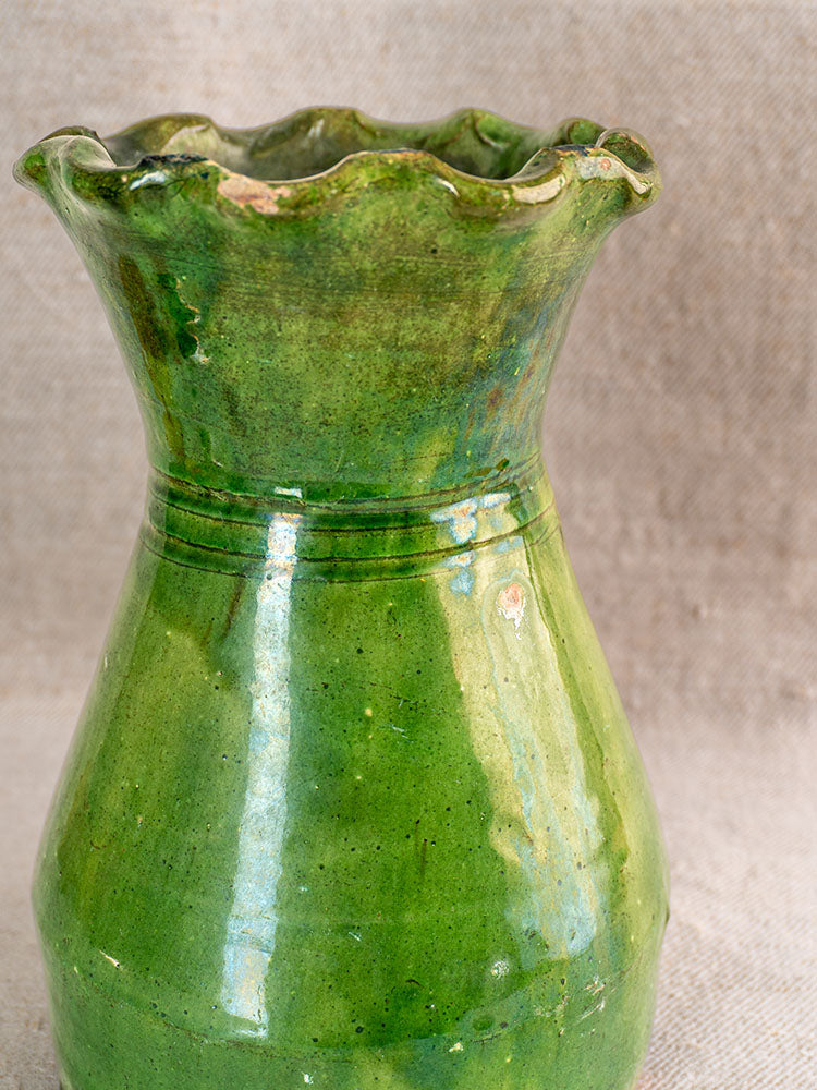 19th century French green glazed terracotta vase with scalloped rim displayed on neutral fabric surface.