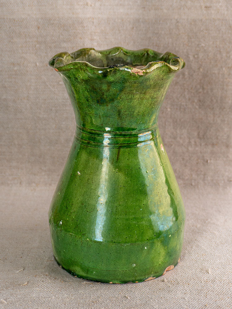 19th-century French green glazed terracotta vase with scalloped rim and vintage patina, shown on beige fabric.