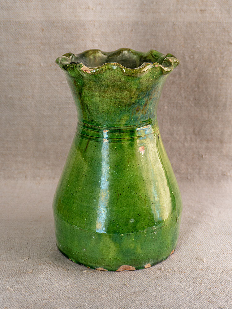 19th century French green glazed terracotta vase with scalloped rim, minor chips near base, on textured beige fabric.