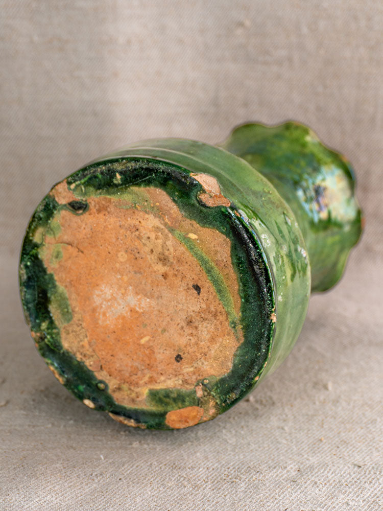 19th century French green glazed terracotta vase with scalloped rim, unglazed base displayed on textured beige fabric.