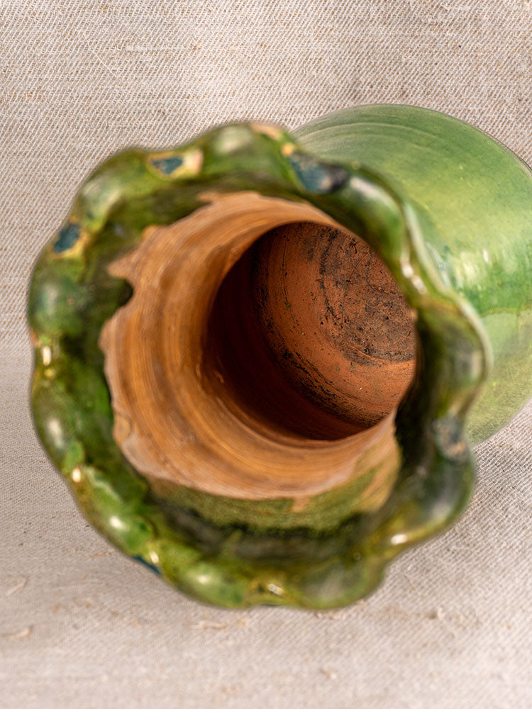 19th century French green glazed terracotta vase with scalloped rim, unglazed interior, on textured beige fabric.