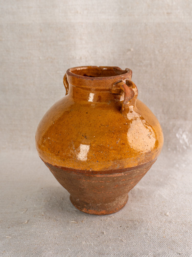 Late 19th-century French olive oil jar, glazed earthenware with brown upper half, rustic unglazed base on beige textured surface.