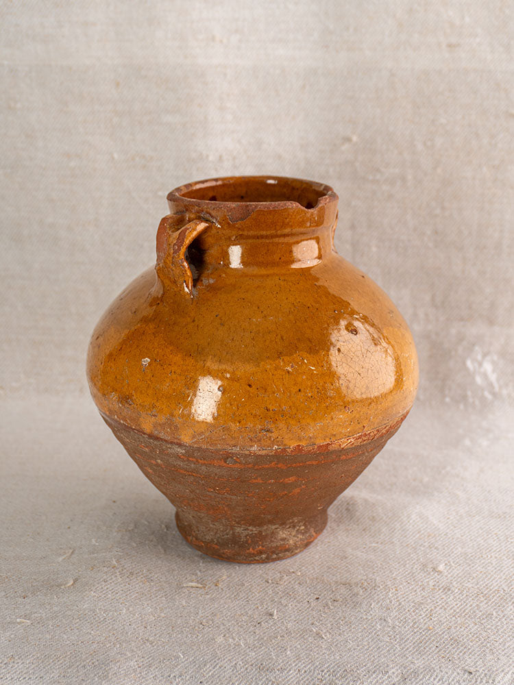 Antique French olive oil jar, late 19th century glazed earthenware, rustic brown finish, on light textured fabric background.