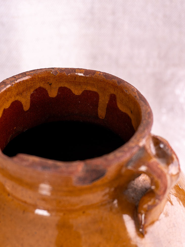 Antique French olive oil jar, late 19th century glazed earthenware, glossy finish, rustic drips, blurred background.