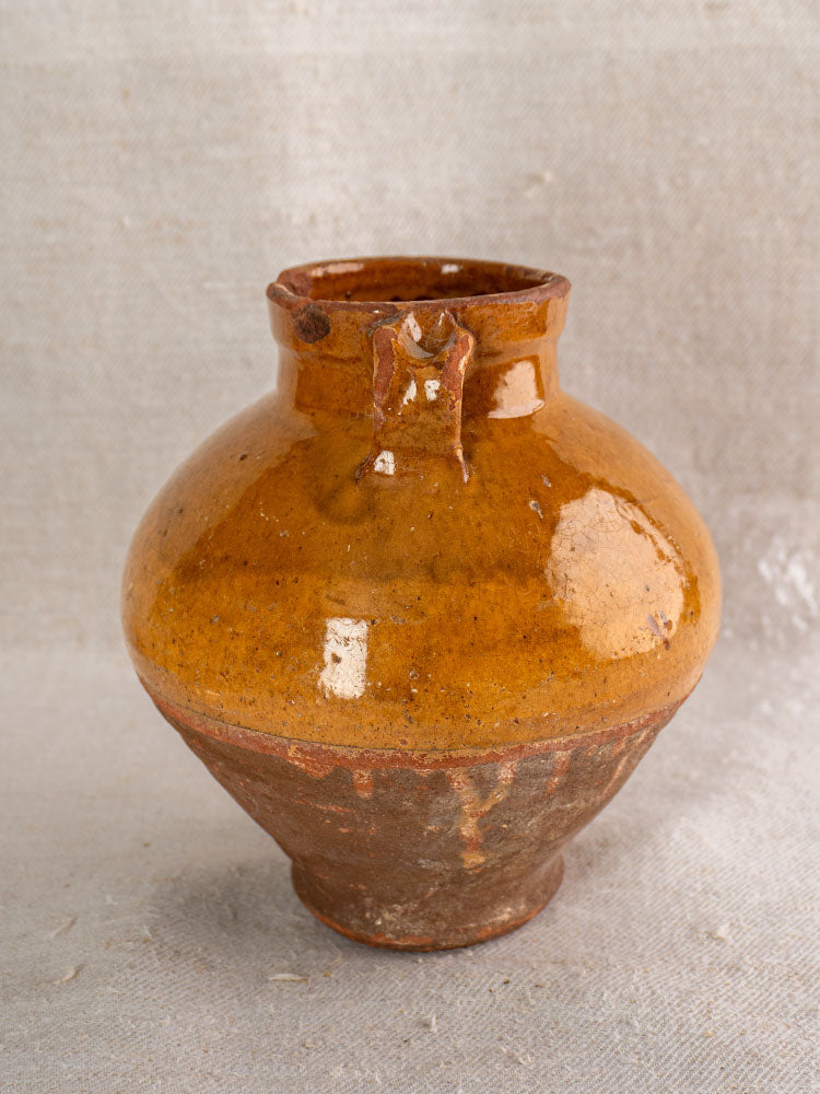 Antique French olive oil jar, glazed earthenware with wide body and narrow neck, on light textured fabric background.