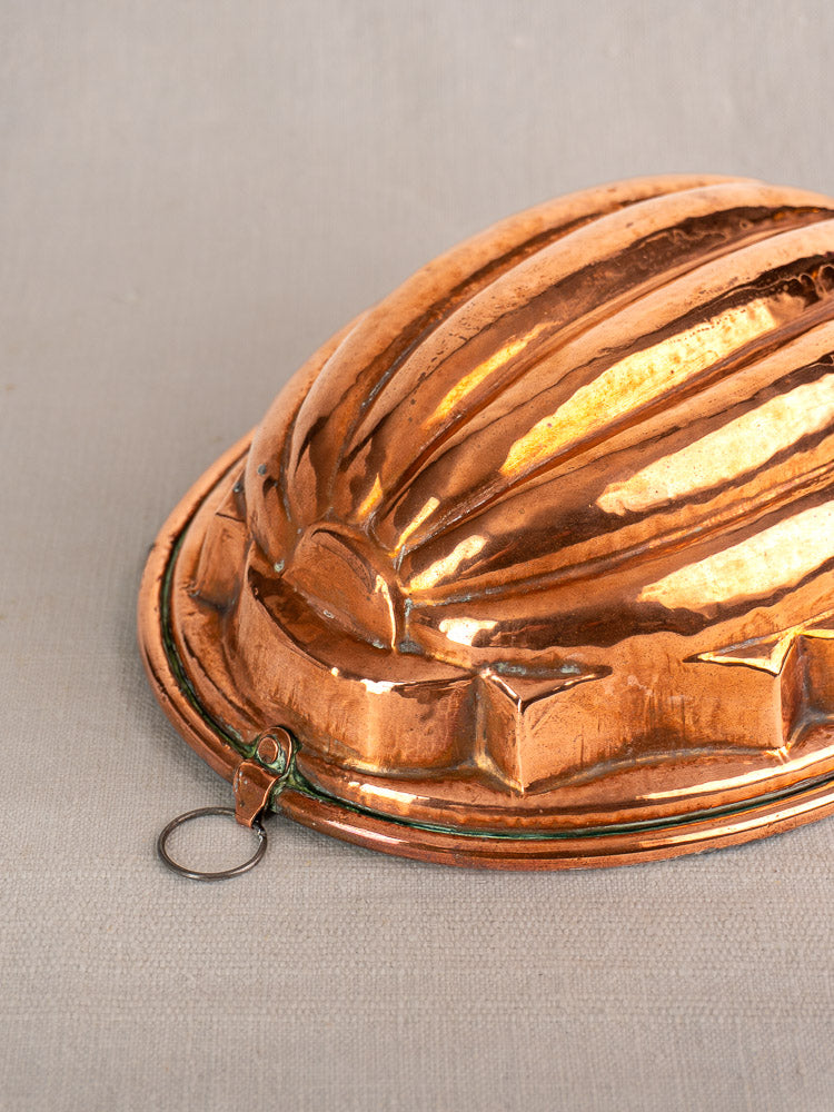 Antique French copper melon mold with fluted dome and hanging ring, tin-lined, on neutral fabric background.