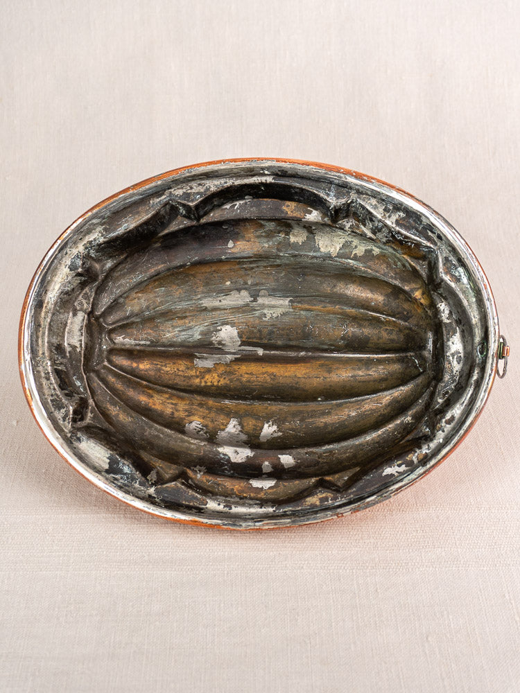 Antique French copper melon mold, tin-lined with ridged pattern, gently worn, on neutral textured fabric background.