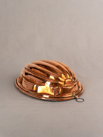 Antique French copper melon mold with fluted ridges and hanging ring on a light-gray surface.