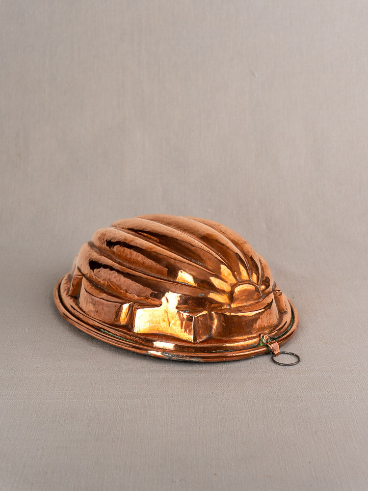Antique French copper melon mold with fluted ridges and hanging ring on a light-gray surface.