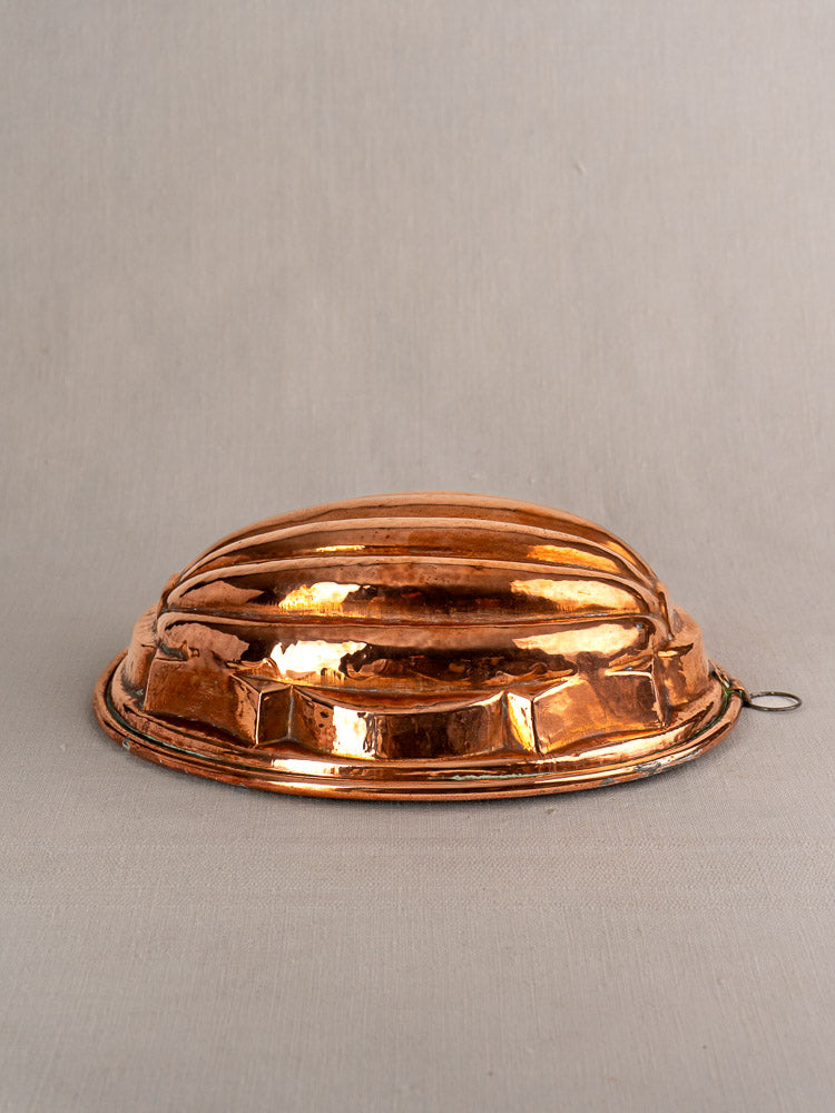 Antique French copper melon mold, tin-lined with a ridged top and hanging ring, on neutral fabric background.