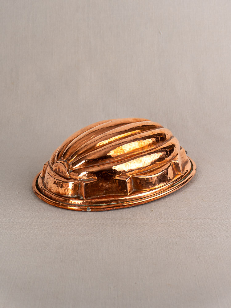 Antique French copper melon mold with ribbed, oval design on a neutral fabric background. Tin-lined interior.