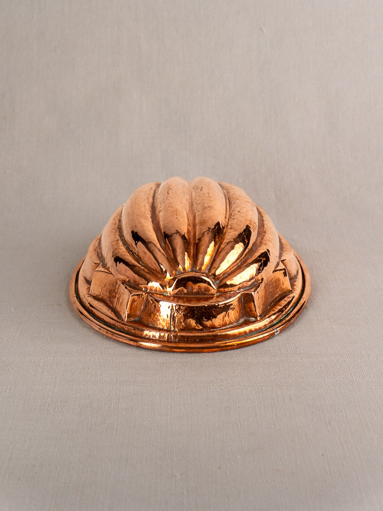 Antique French copper melon mold with fluted design, tin-lined, displayed upside down on a light fabric surface.