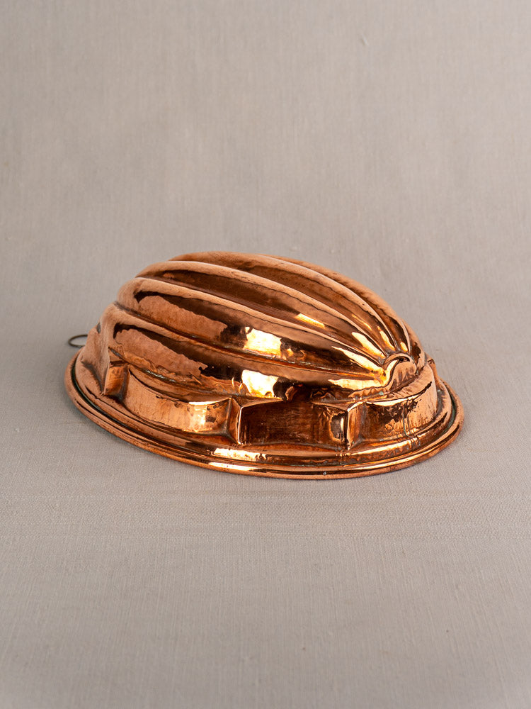 Antique French copper melon mold with tin lining and ridged dome shape on light beige fabric background.