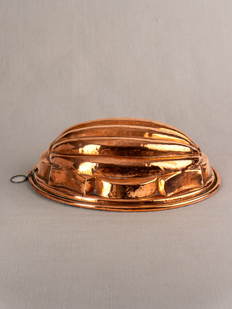 Antique French copper melon mold with tin lining, rounded fluted shape, and hanging loop on a neutral surface.