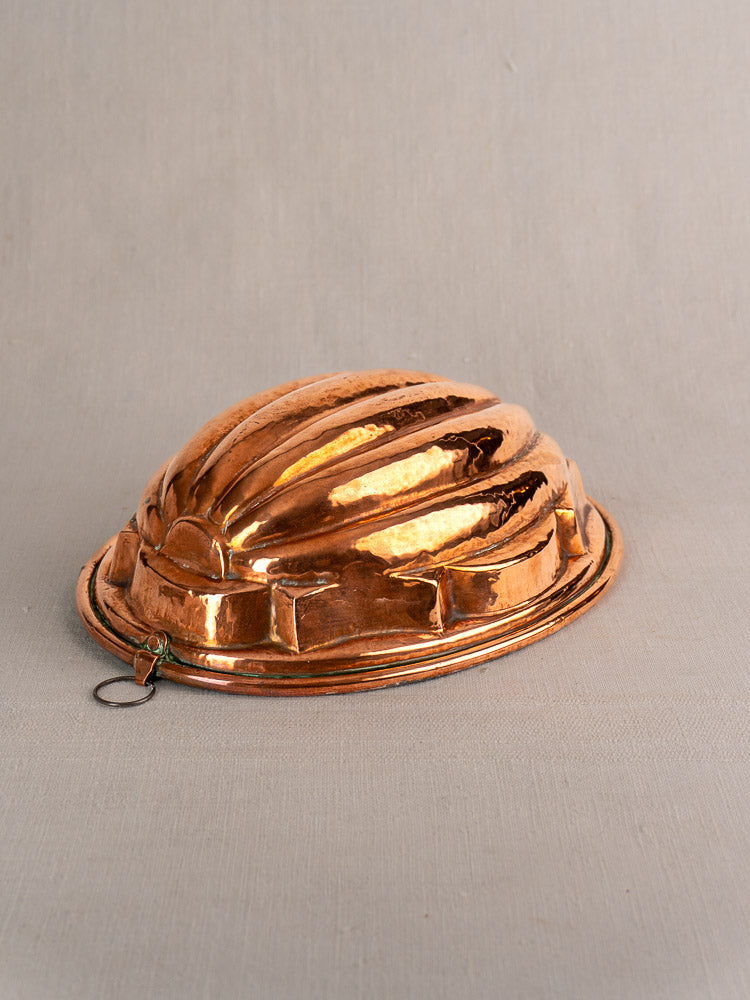 Antique French copper melon mold, tin-lined oval with fluted ridges and hanging ring, on neutral fabric backdrop.