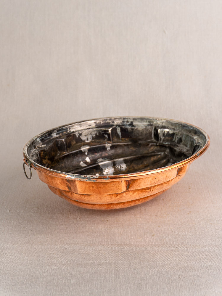 Antique French copper melon mold with tin lining, tarnished interior, and hanging ring, on neutral fabric background.