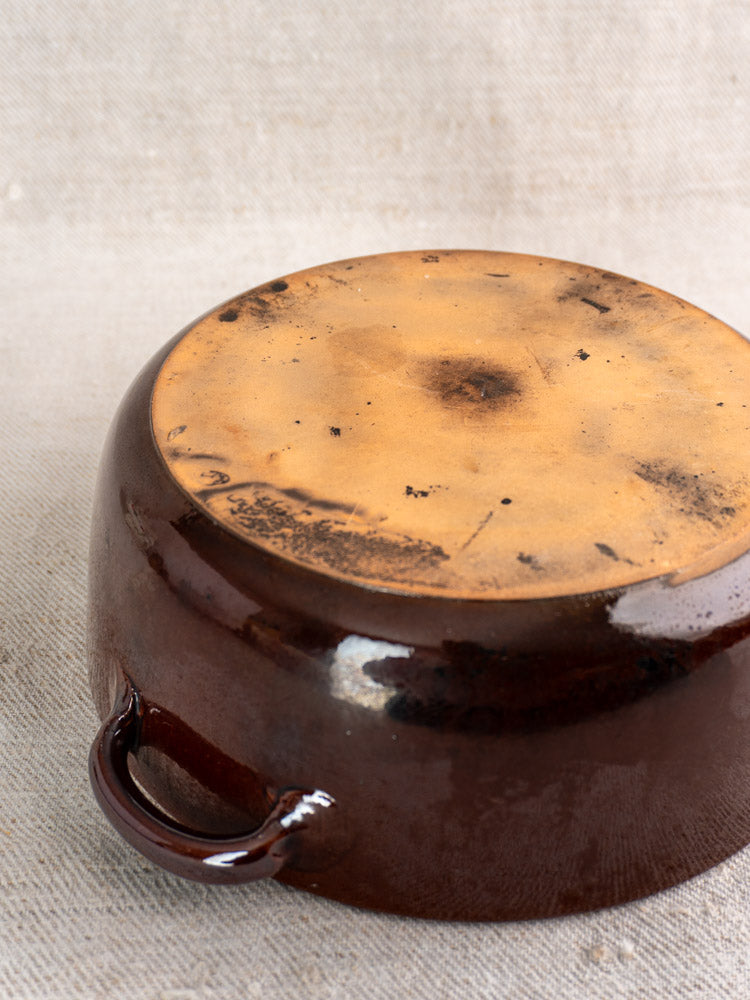 Mid-century French earthenware baking dish with brown-orange glaze, shown upside down on textured beige fabric.