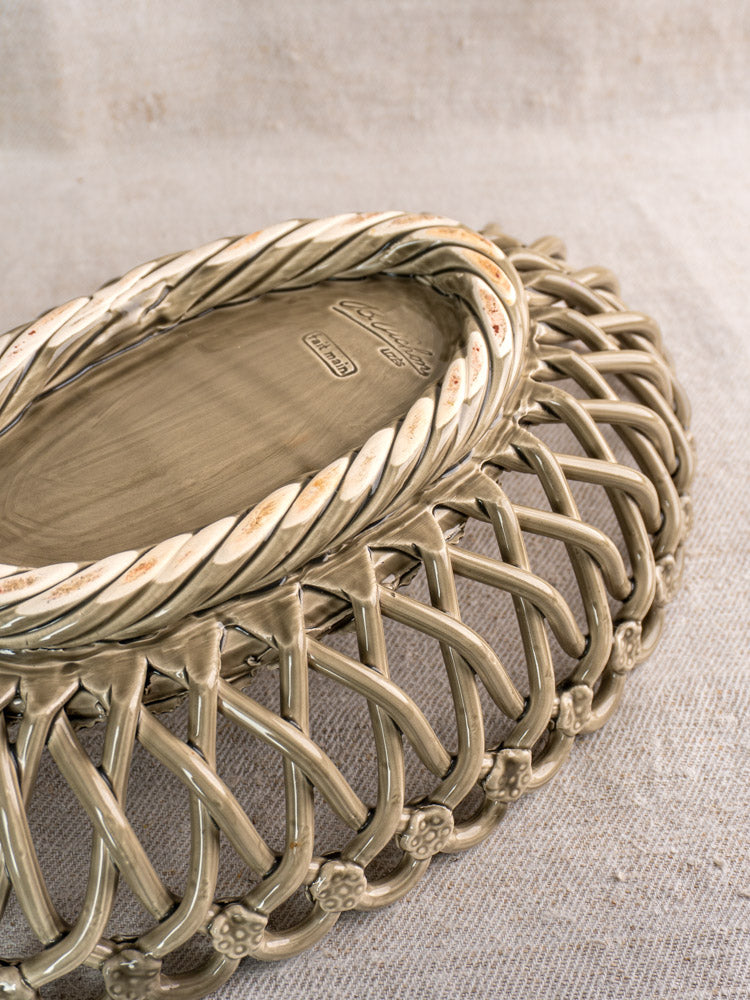 Large vintage Pichon Uzès faience basket, oval with twisted rim and lattice design, stamped base on neutral textured fabric.