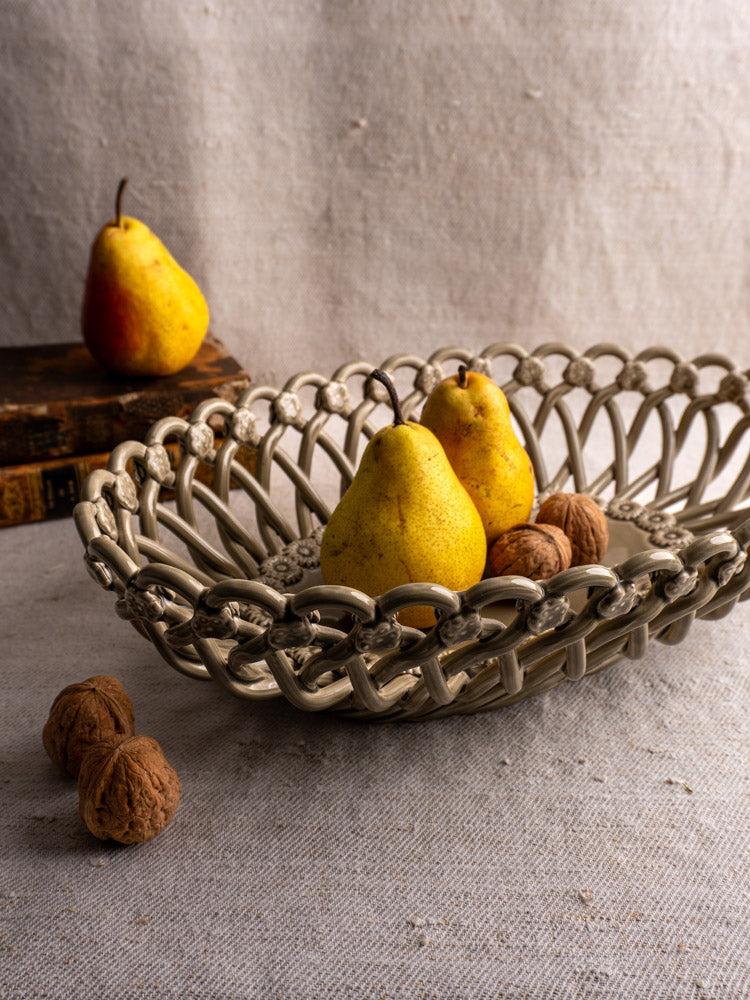 Large vintage Pichon Uzès oval ceramic basket with pears and walnuts on a textured beige surface, books nearby.