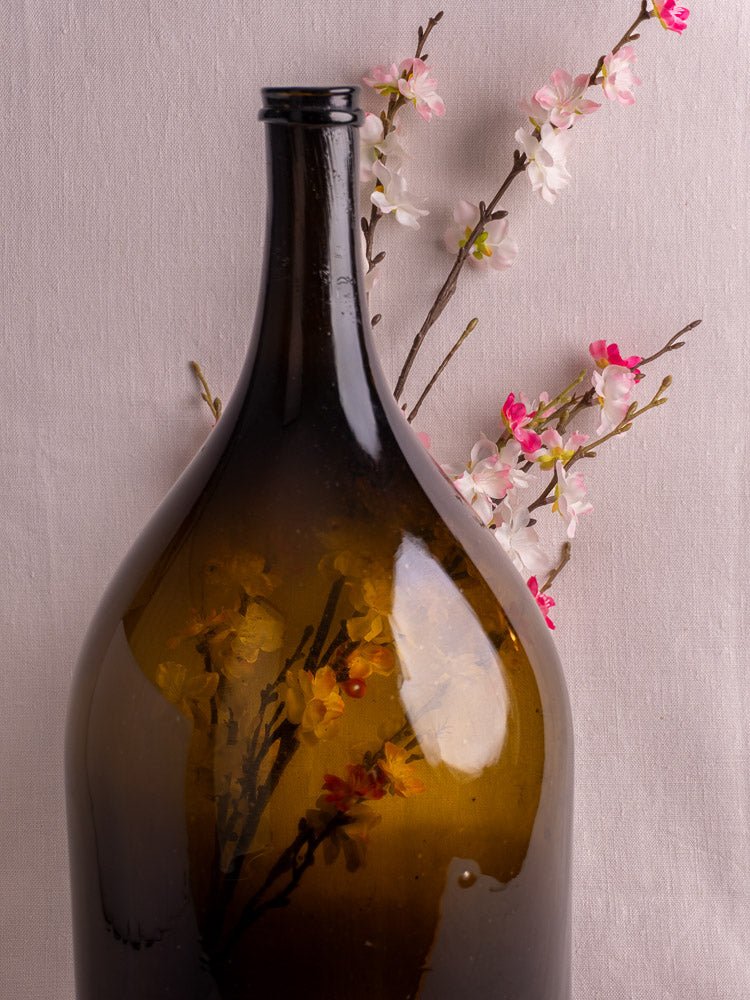 19th century French hand blown olive green glass wine bottle with cherry blossom branches and soft fabric backdrop.