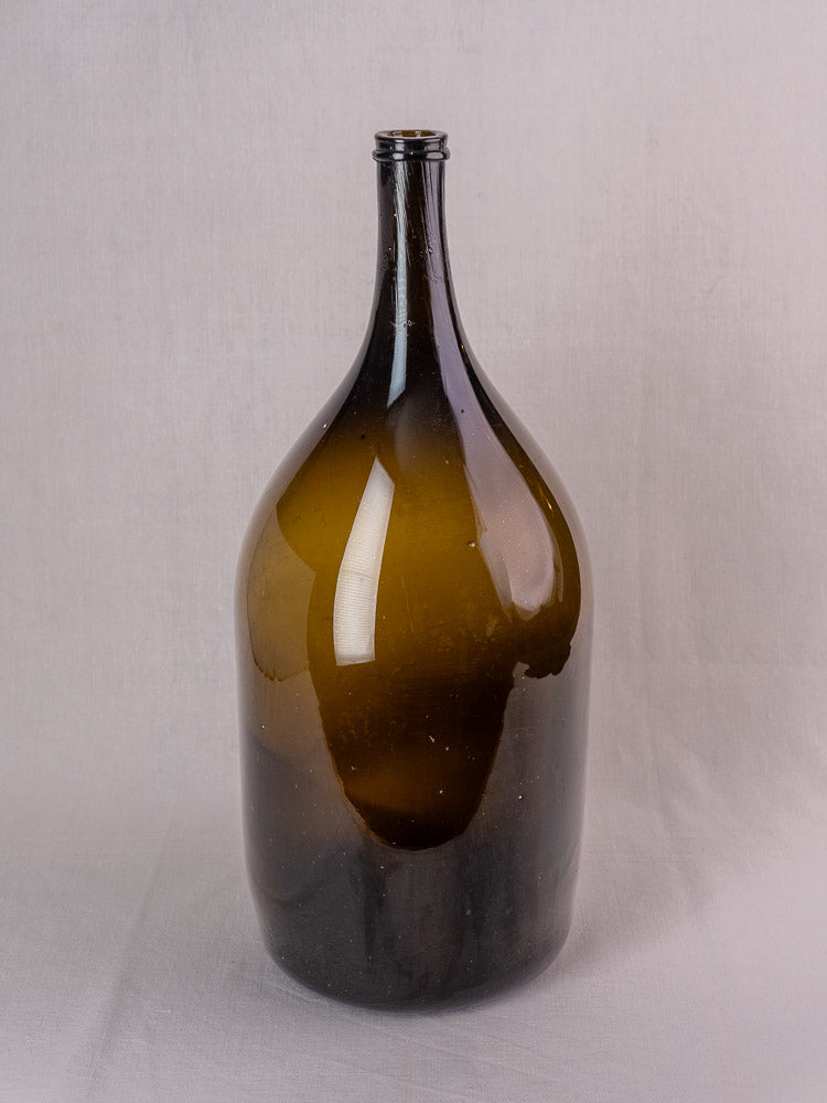 Antique 19th-century French hand-blown olive green glass wine bottle on a light background.