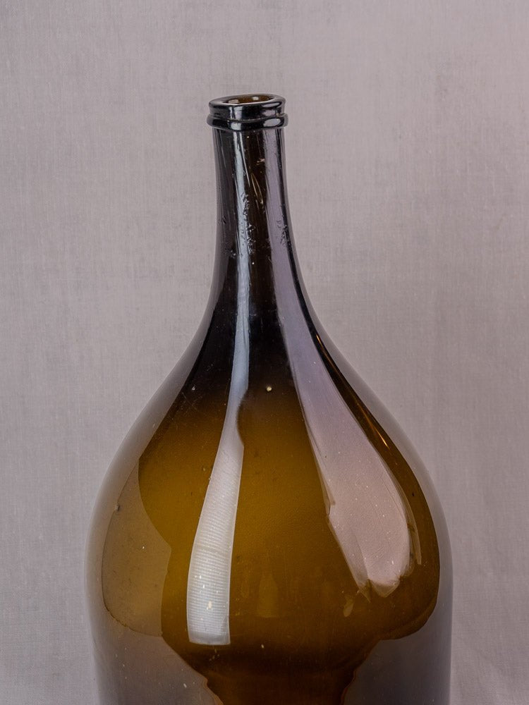 Antique French 19th-century hand-blown olive green glass wine bottle on a light gray background.