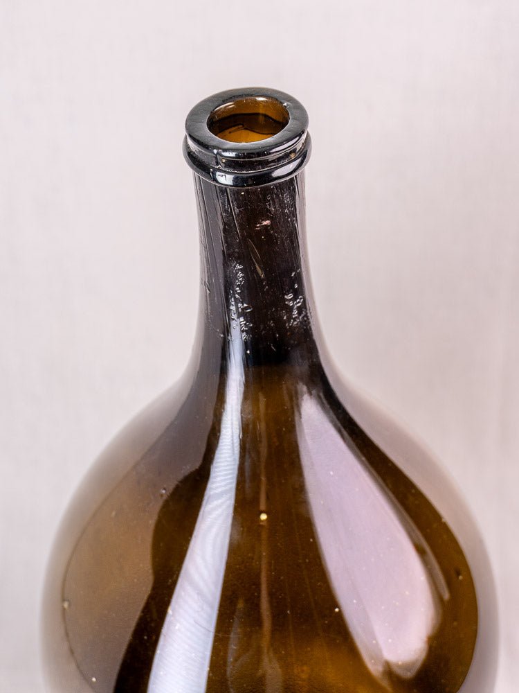Antique French hand blown olive green glass wine bottle with narrow neck on a light background.